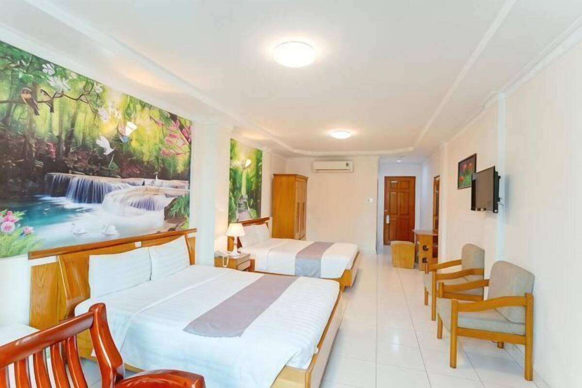 A hotel room with two beds, a wooden chair, a desk, and a painting of a waterfall.