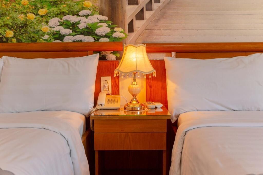 A hotel room with two beds, a nightstand with a lamp, a telephone, and a small table.