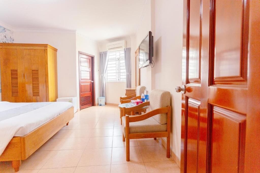 Habitación de hotel con cama, armario de madera, escritorio con silla, televisor y ventana con cortinas.