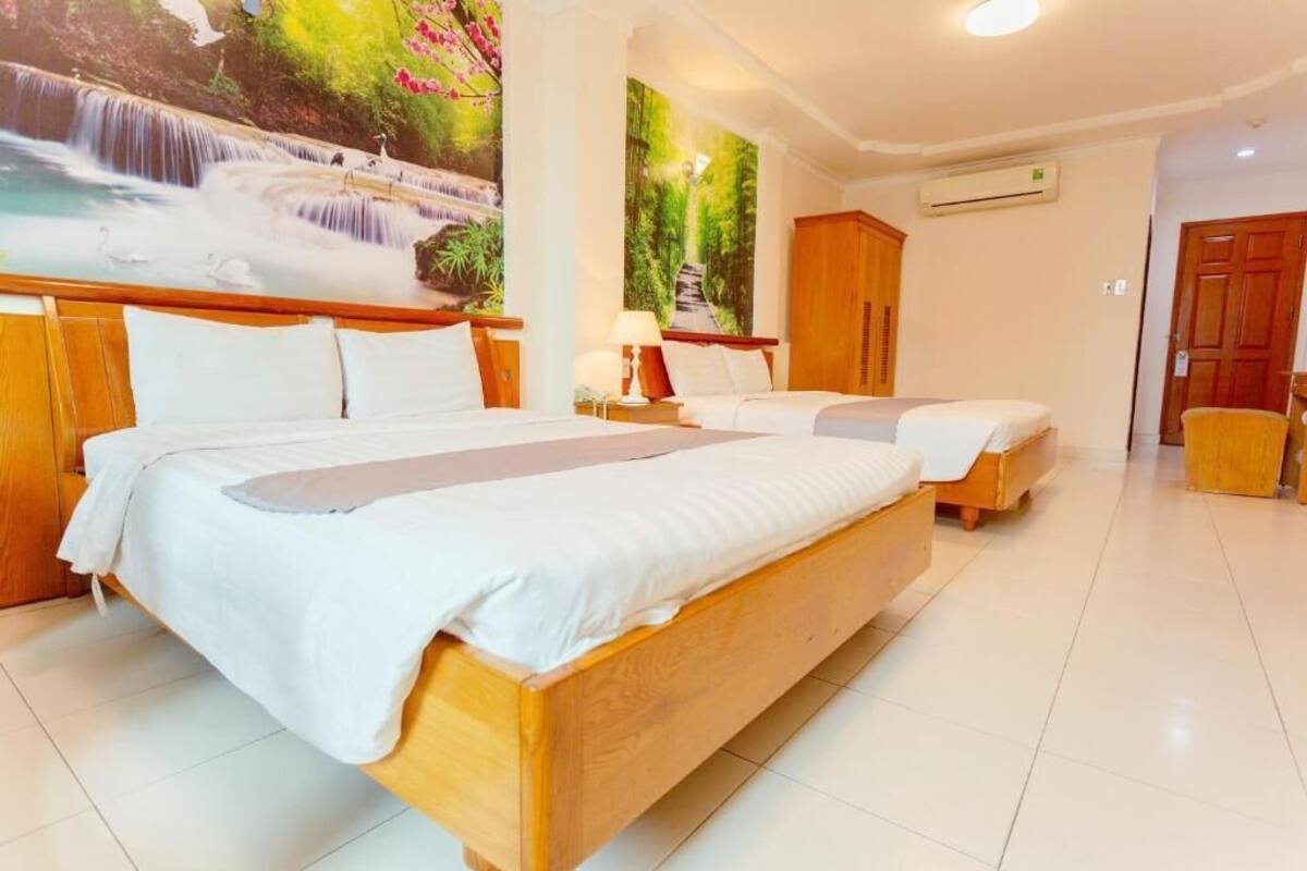 A hotel room with two wooden beds, a large mural of a waterfall, a wooden wardrobe, and a tiled floor.