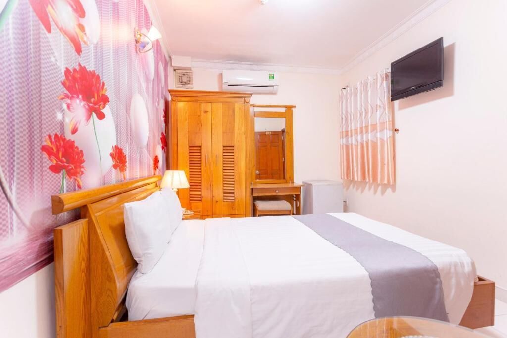 A hotel room with a bed, a desk, a wardrobe, an air conditioner, and a television.
