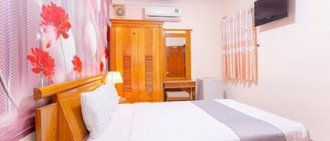 A hotel room with a bed, a desk, a wardrobe, an air conditioner, and a television.