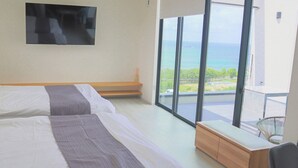 Een slaapkamer met twee bedden, een bankje, een televisie en een balkon met uitzicht op de oceaan.