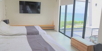 Un dormitorio con dos camas, una banca, televisión y balcón con vista al océano.