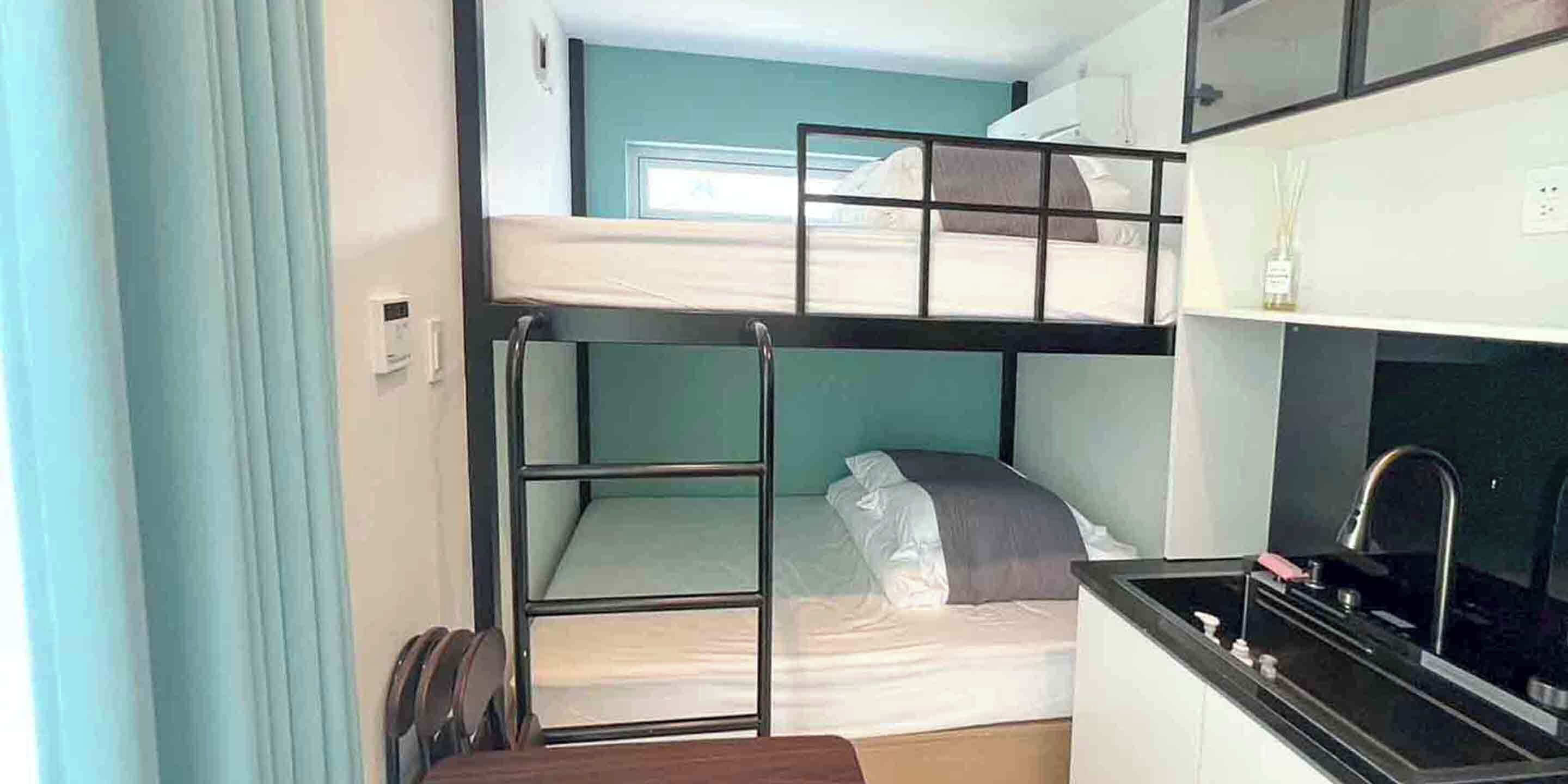 A bunk bed with a kitchenette below, a window with curtains, and a small table.