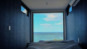 Een slaapkamer met een groot raam, met uitzicht op zee en een eiland in de verte.