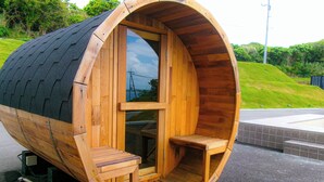 Een houten sauna met een gebogen dak, een bankje binnenin en een deur naar de binnenruimte.