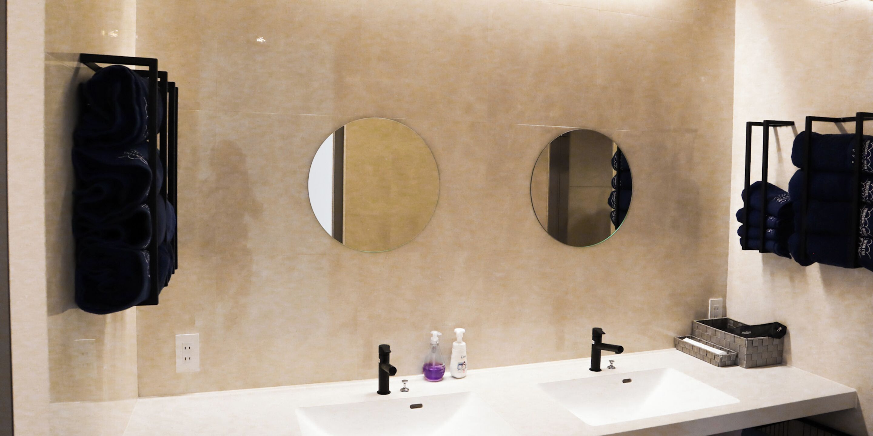 A bathroom with two sinks, a large mirror, and a towel rack with folded towels.