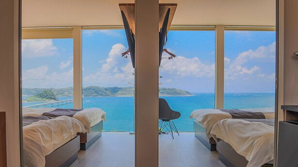 Een slaapkamer met twee bedden, een groot raam en uitzicht op zee.