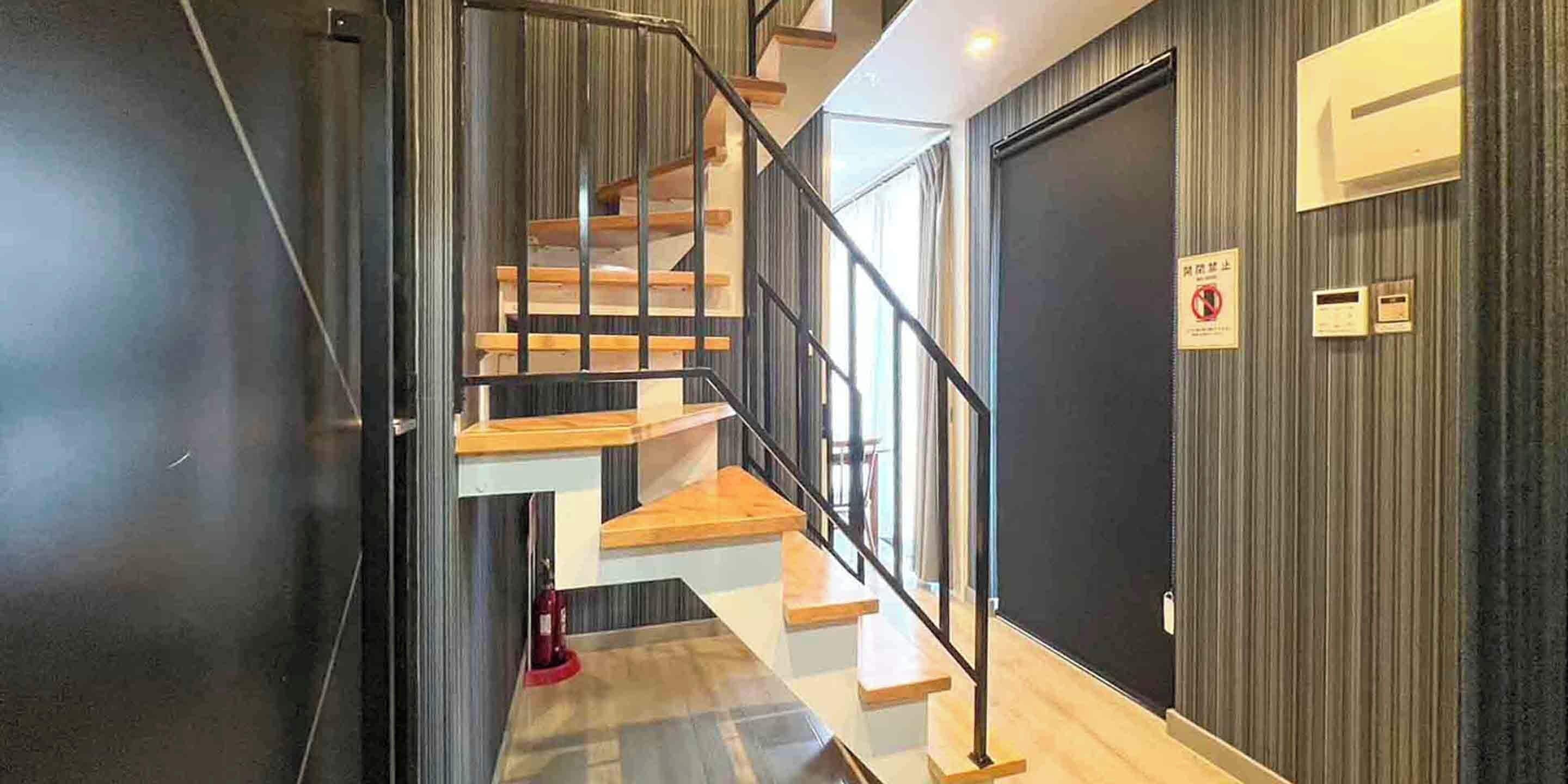 A modern staircase with wooden steps and metal railings, leading to a room with a dark wall and a door.