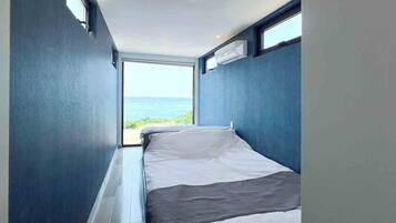 A narrow room with a bed, a window, and an air conditioning unit.