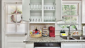 Una cocina con gabinetes blancos, encimera de granito, cafetera y fregadero.