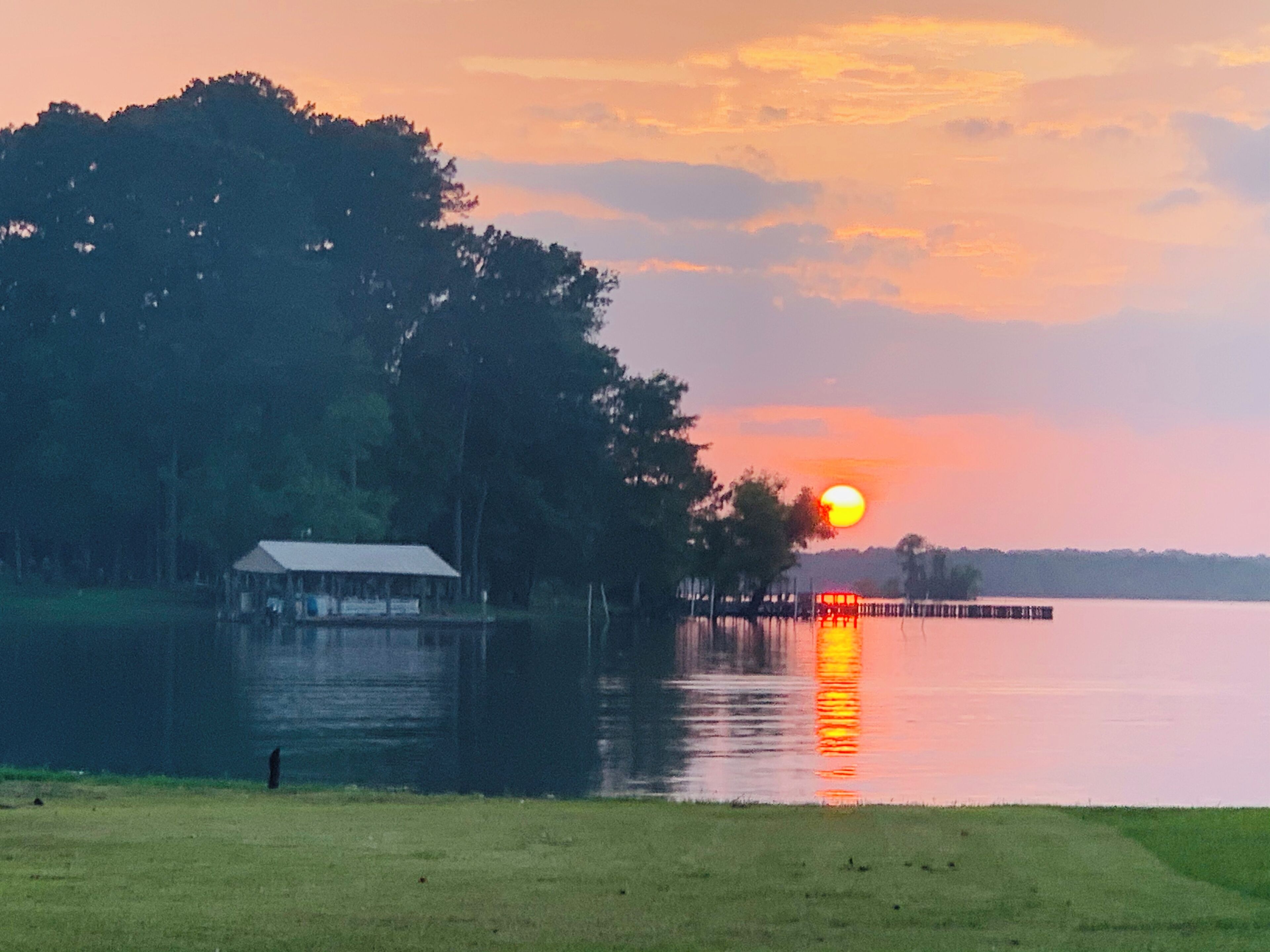 A lakeside view with a dock extending into the water, a small building near the shore, and a sunset in the background.