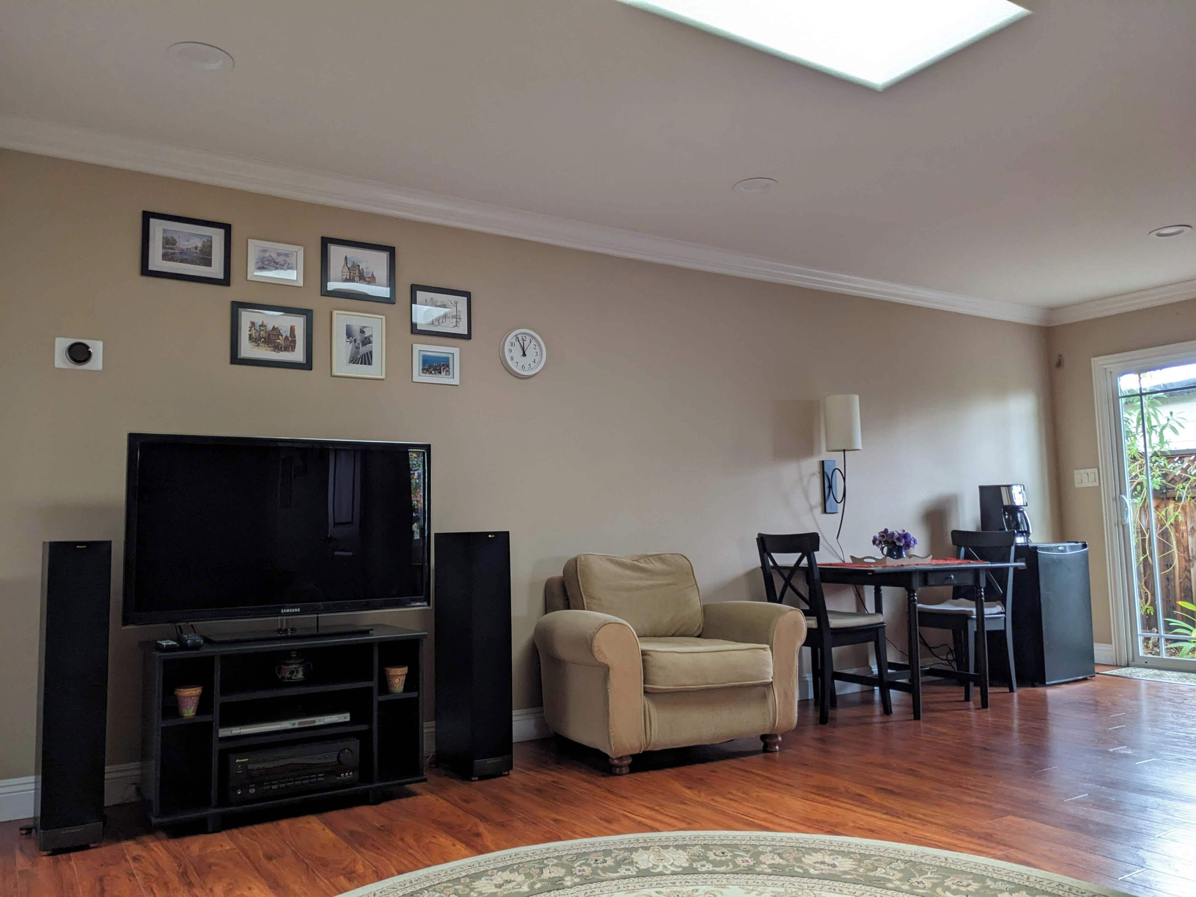A living room with a flat-screen TV, a beige armchair, a dining table with chairs, and a coffee table.
