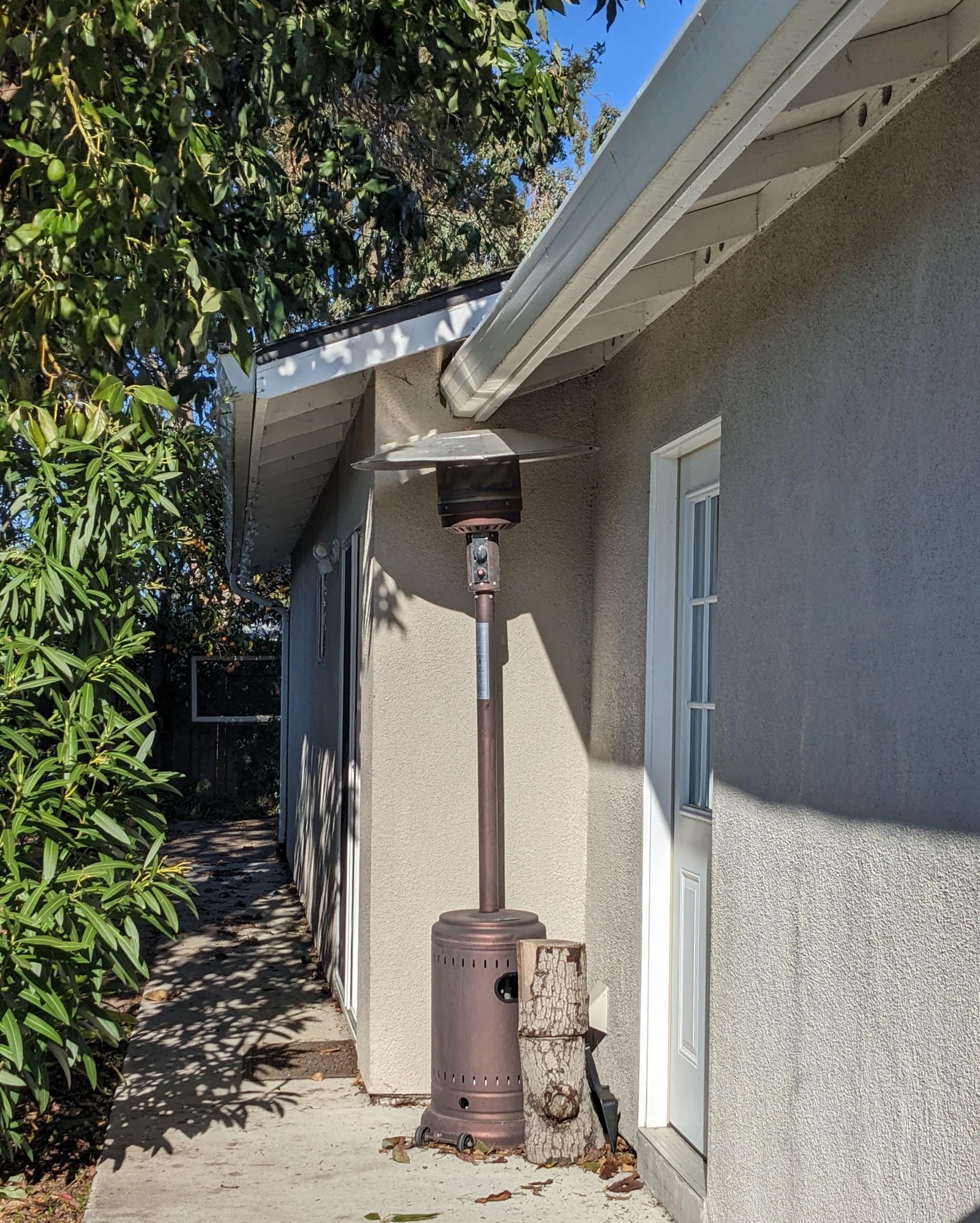 A patio area with a wood-burning stove, a concrete pathway, and a house with a white door and window.