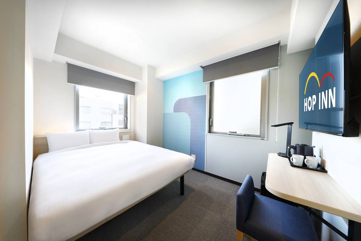 A modern hotel room with a bed, a desk with a coffee maker, and a TV.