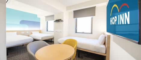 A modern hotel room with a bed, a sofa, a table, and a chair. There is a window with a view of the sky and a wall-mounted screen displaying the hotel name.