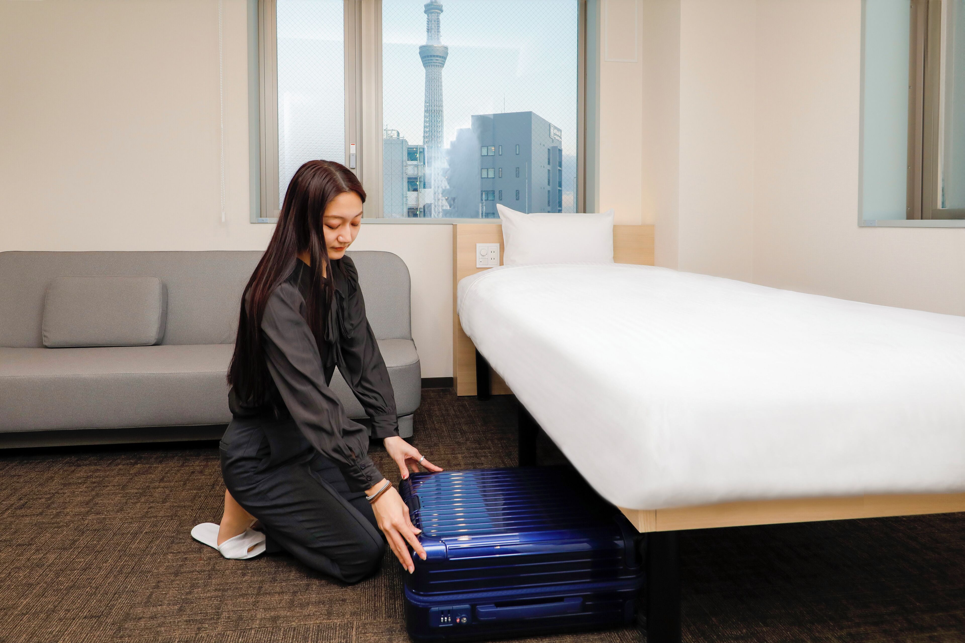 A hotel room with a bed, a sofa, and a view of a tower through a window.