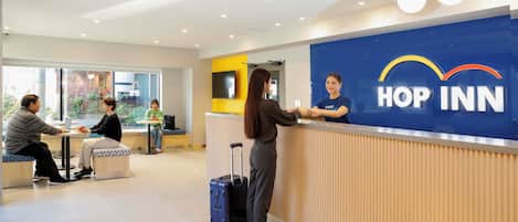 A reception area with a blue wall displaying the "HOP INN" logo, a counter, and seating areas with tables and chairs.