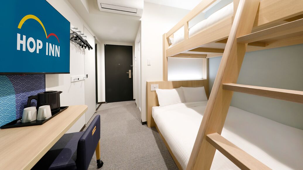 Quarto com beliche, uma escrivaninha e um letreiro 'HOP INN'.