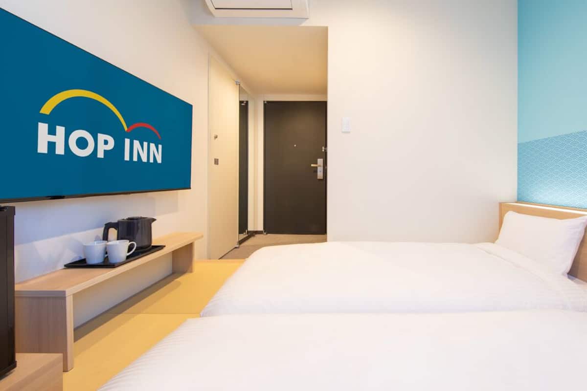 Una habitación de hotel con una cama, un televisor montado en la pared, una cafetera y una puerta que da a otra habitación.
