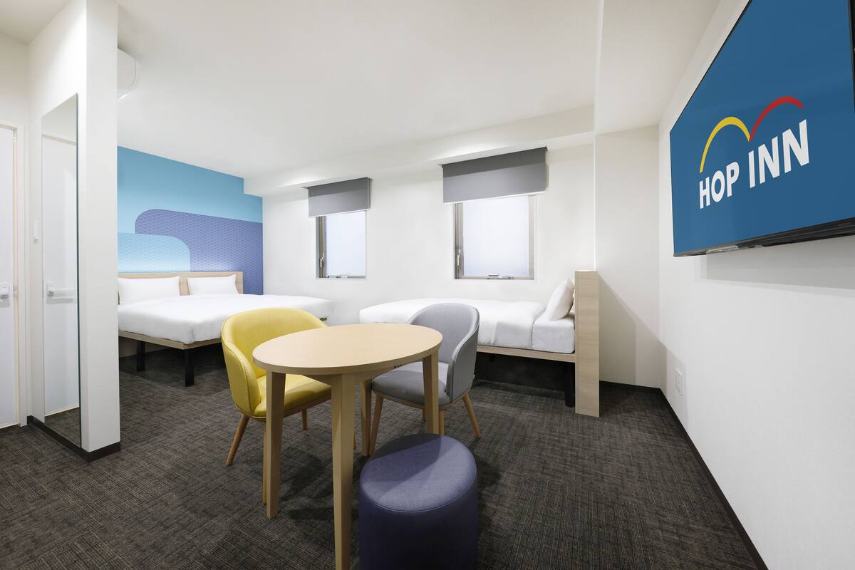 A modern hotel room with a bed, two seating areas, a small table, and a wall-mounted sign.