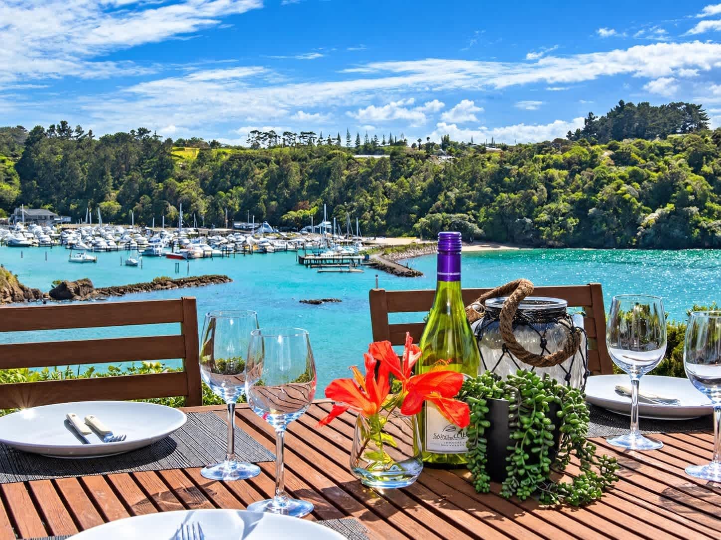 A table set for dining with a view of a marina and forested hills.