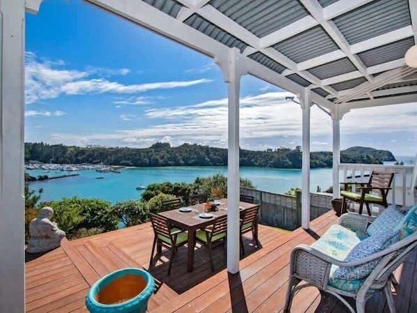 A covered outdoor deck with a table and chairs, overlooking a body of water and a marina.