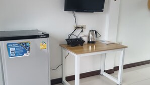 Una habitación con refrigerador, una mesa con tetera y televisor instalado en la pared.