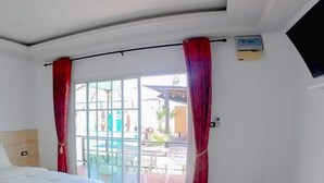 Habitación de hotel con cama, ventana con cortinas rojas y vista a un espacio exterior.