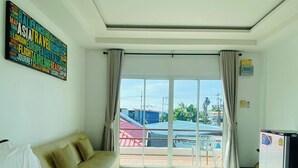 Habitación de hotel con cama, sofá, televisión y balcón con vistas a edificios.