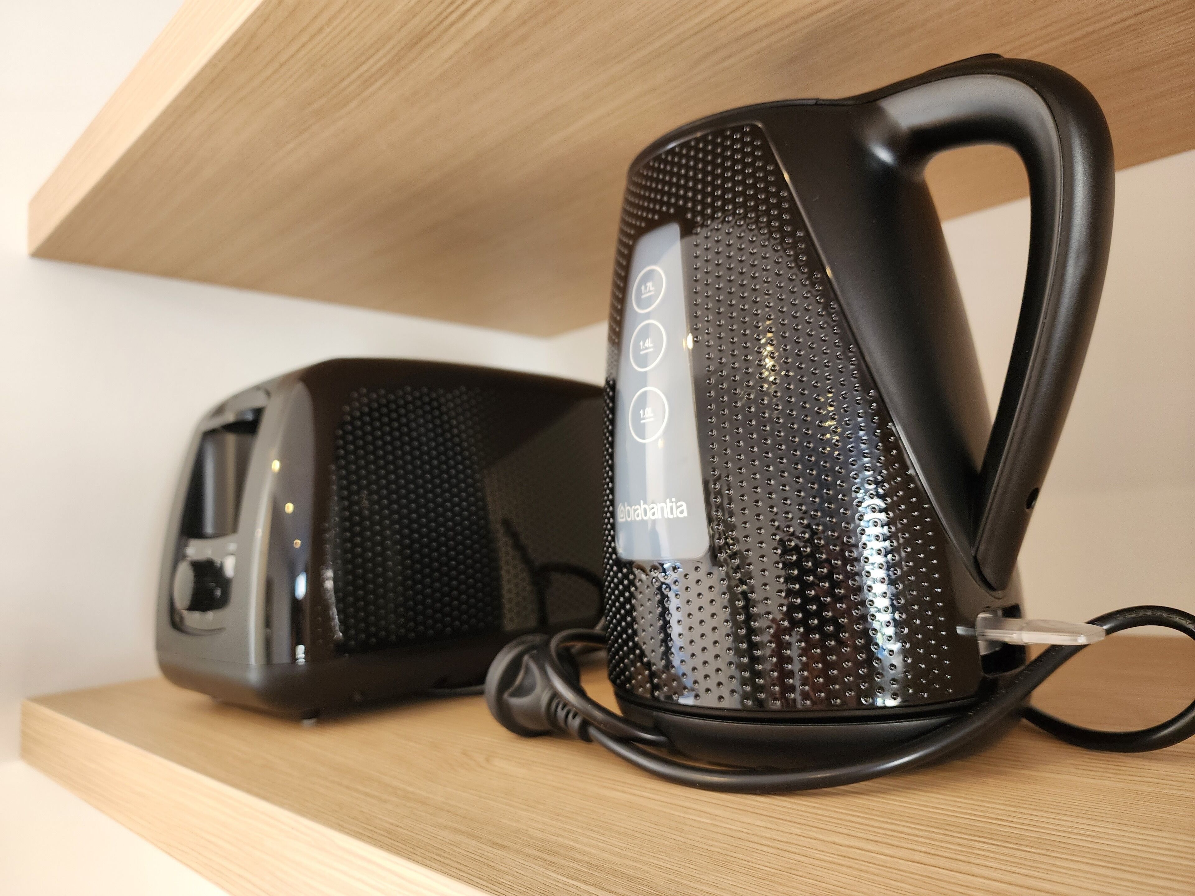 A black portable speaker with a textured surface and a brand label, placed on a wooden shelf.