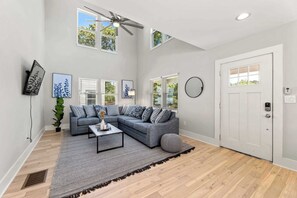 A living room with a sectional sofa, a coffee table, a ceiling fan, and a door with a keypad lock.