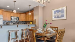 A kitchen with wooden cabinets, a microwave, and a dining area with a round table and chairs. - Best Views of Canmore - 2Bed 2Bath (Canmore)