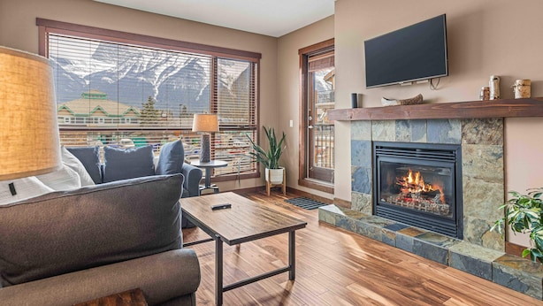 A living room with a fireplace, a sofa, a coffee table, and a TV mounted on the wall. - Best Views of Canmore - 2Bed 2Bath (Canmore)