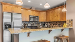A kitchen with wooden cabinets, stainless steel appliances, a granite countertop, and two wooden stools. - Best Views of Canmore - 2Bed 2Bath (Canmore)
