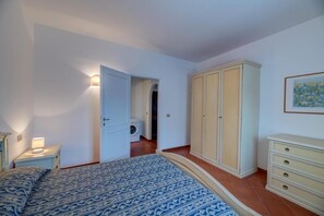 Une chambre à coucher avec un lit, une table de chevet, une armoire et une machine à laver à l’arrière-plan.