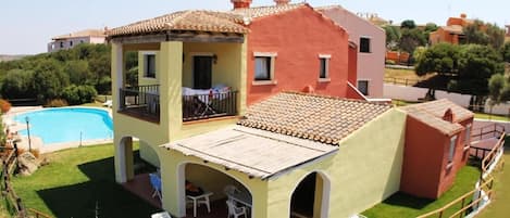 Una casa de dos pisos con piscina, patio cubierto y jardín cercado.