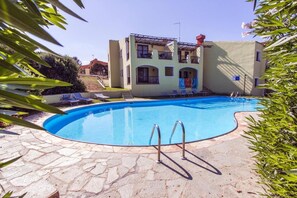 A swimming pool with a stone deck, a two-story building with balconies, and a clear sky.