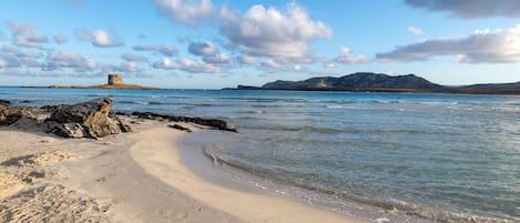 A beach with clear water, a sandy shore, and a distant rocky island.