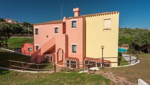 A two-story building with a red and yellow facade, a staircase, and a pool area. - Charming Sea & Villas Villa and Extra Bed possible num2104 (Stintino)