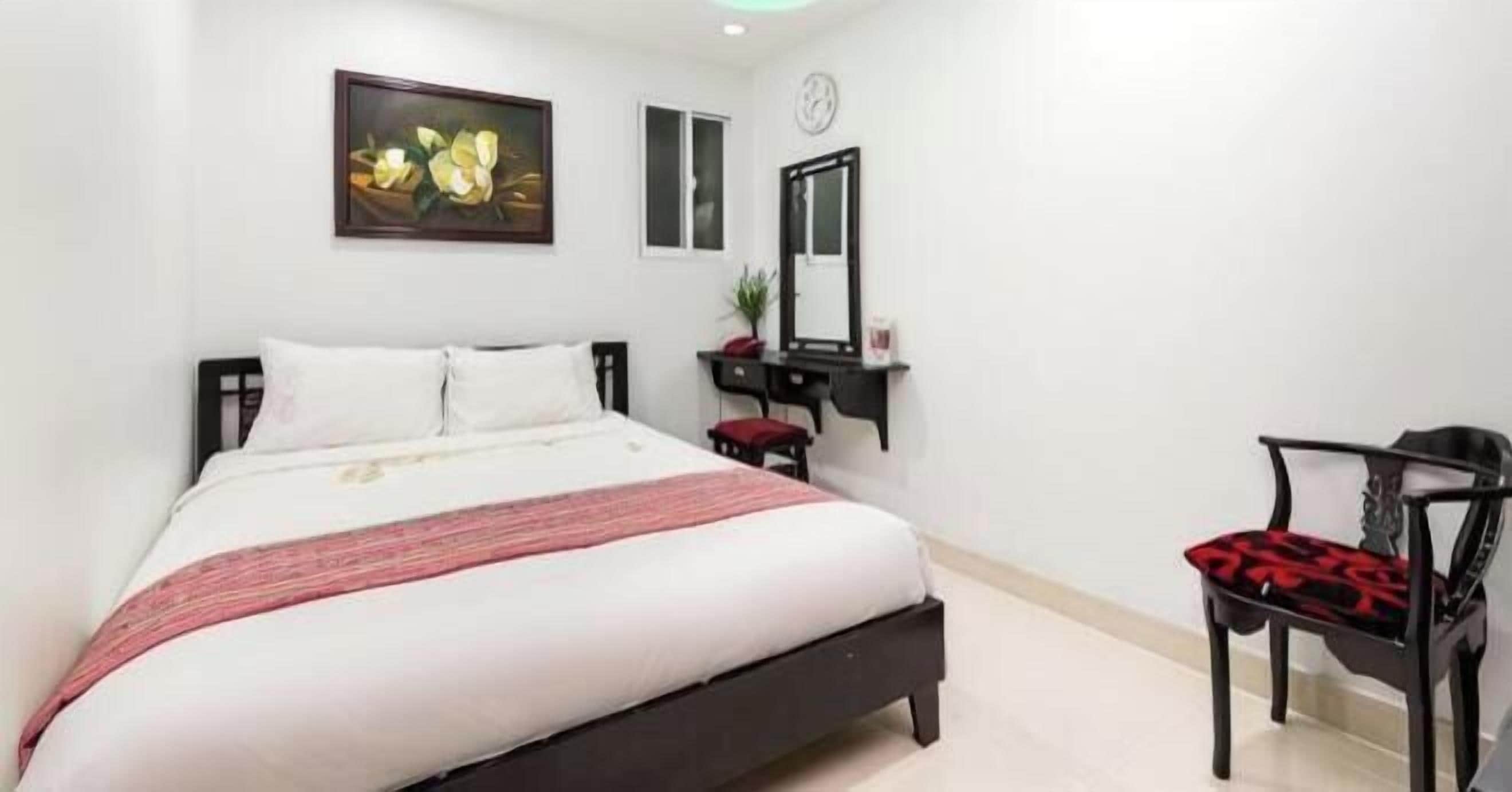 A hotel room with a bed, a desk with a chair, a mirror, and a painting on the wall.