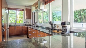 A modern kitchen with wooden cabinets, a large island, and a coffee maker. - Luxury Matahari Seaview (Kamala)
