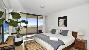 A modern hotel room with a large bed, a potted plant, a desk with a computer, and a balcony with a view. - Freddie's at St Tropez (The Entrance)