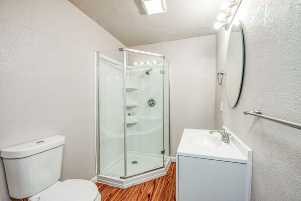 Un baño con ducha de vidrio, inodoro y lavamanos con espejo.