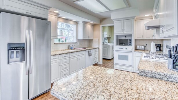 A modern kitchen with stainless steel appliances, white cabinetry, and a granite countertop.