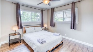 A bedroom with a bed, two bedside tables with lamps, a ceiling fan, and windows with curtains.