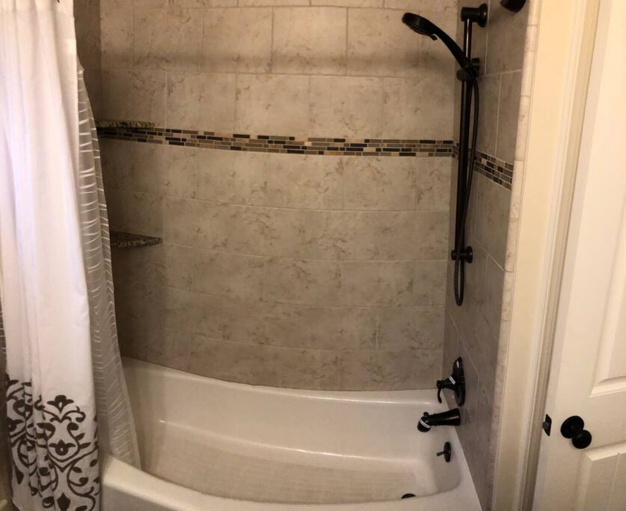 Une douche équipée d’un pommeau de douche à main, d’un robinet mural et d’un sol carrelé.