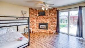 A room with a brick fireplace, a ceiling fan, a bunk bed, and a sliding glass door to the outside.