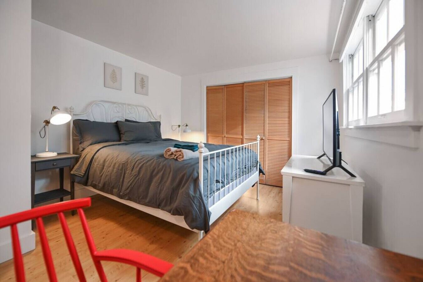 A bedroom with a bed, bedside table, lamp, wooden wardrobe, and a TV stand.